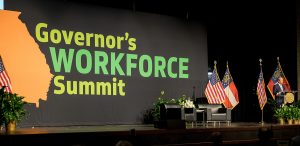 Georgia Governor Brian Kemp speaking on a stage with the Governor's Workforce Summit logo in the background